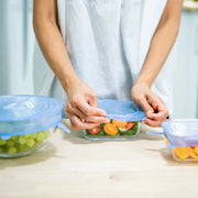 Person preparing a salad with silicone lids on glass containers.