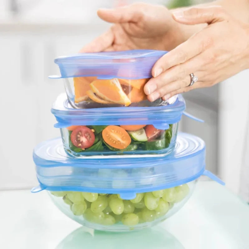 Stack of glass food containers with silicone lids containing fruits and vegetables.