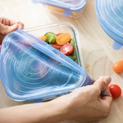 Person holding a blue silicone lid over a container of salad on a wooden surface.
